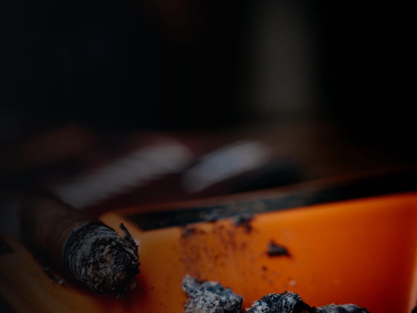 A lit cigar resting on an orange ashtray